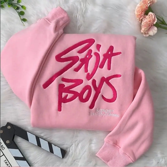 Pink hoodie with 'Saja Boys' text on a white surface with flowers