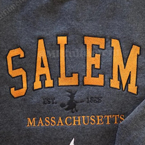 Gray sweatshirt with 'Salem, Massachusetts' text and witch hat design on a white surface.