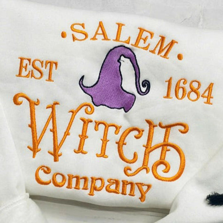 White pillow with 'Salem Est 1684 Witch Company' text and purple witch hat design on a light wooden surface.