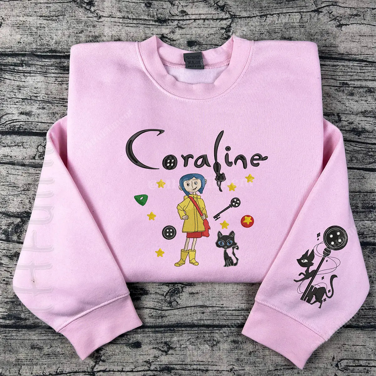 Pink sweatshirt with 'Coraline' design on a wooden surface