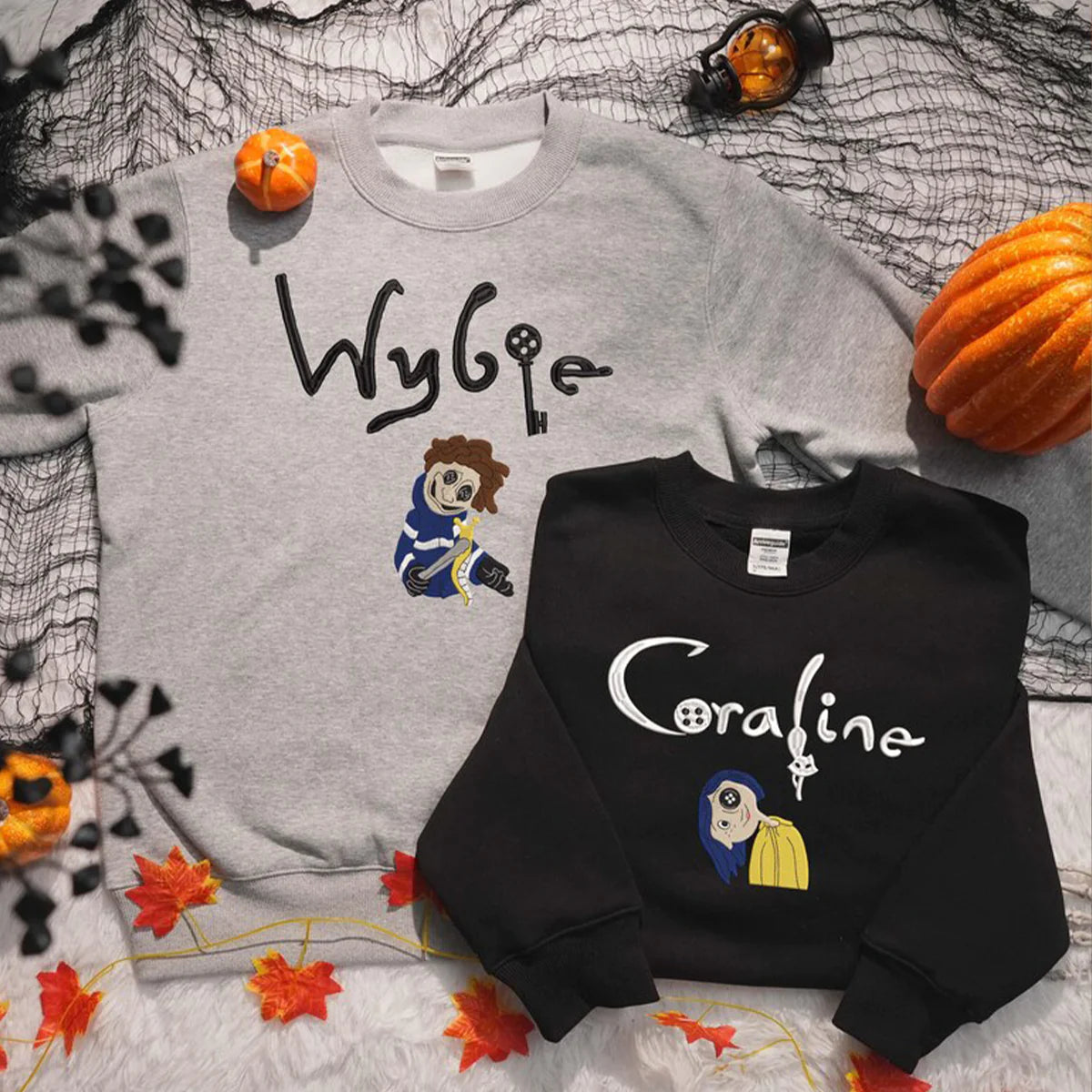 Gray and black sweatshirts with 'Wybie' and 'Coraline' text and character designs on a Halloween-themed background.