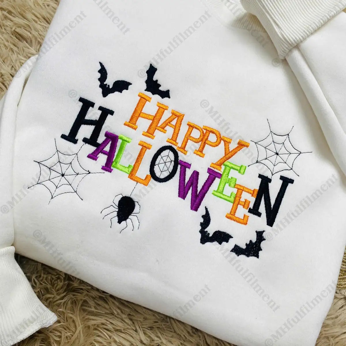 White sweatshirt with colorful 'Happy Halloween' text and spider web designs on a textured surface.