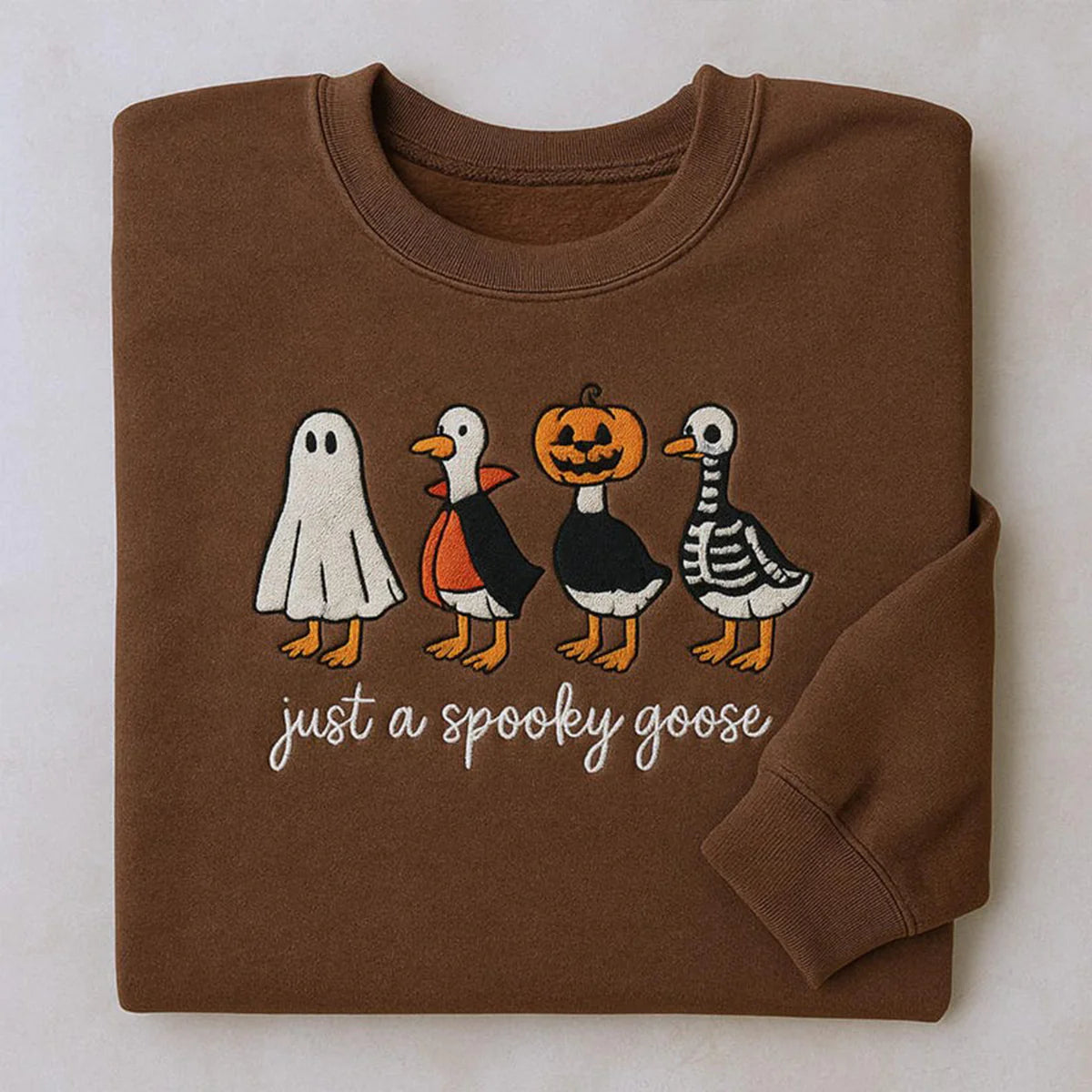 Folded brown sweatshirt with Halloween-themed goose illustrations and text on a light background