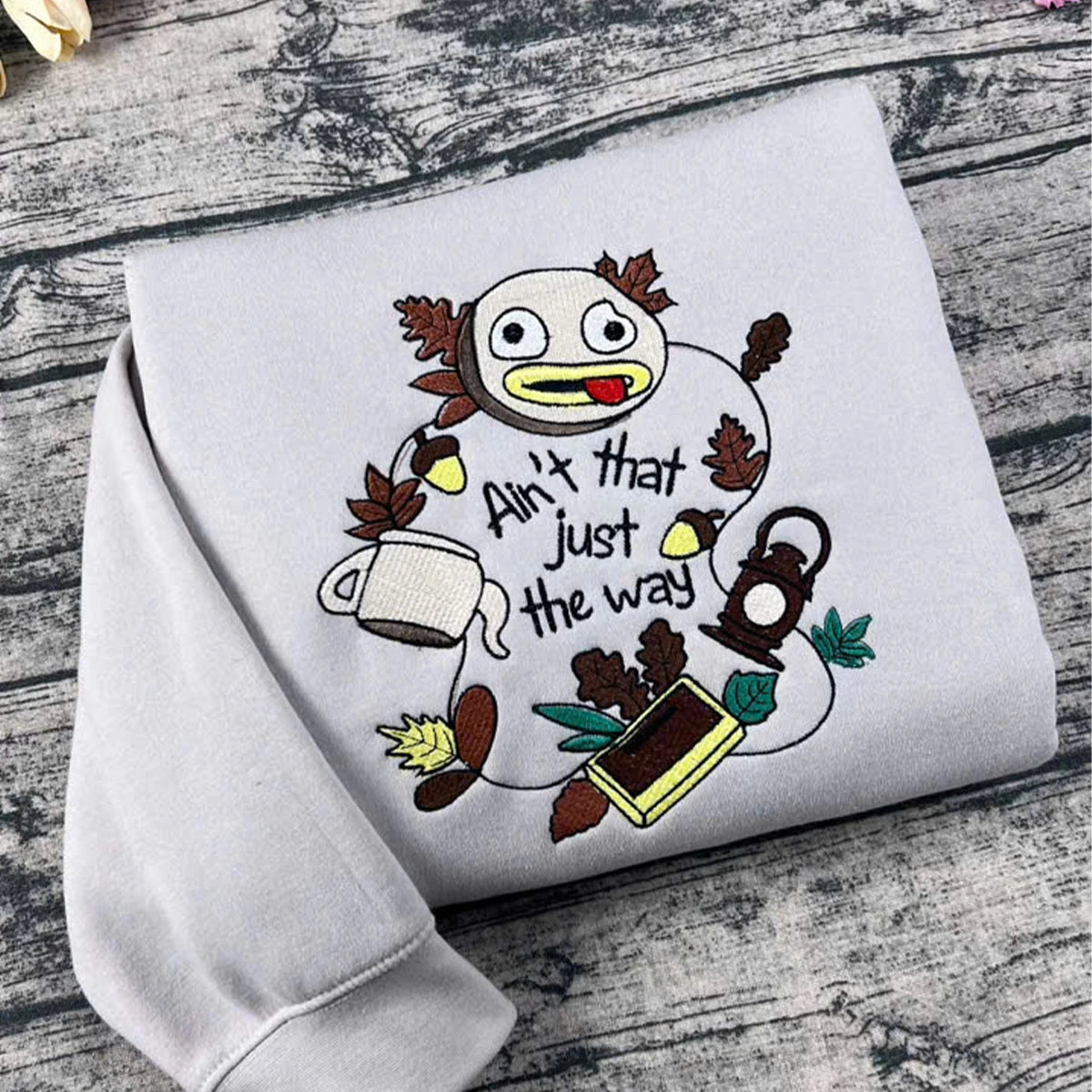 White sweatshirt with cartoon character and text on a wooden surface
