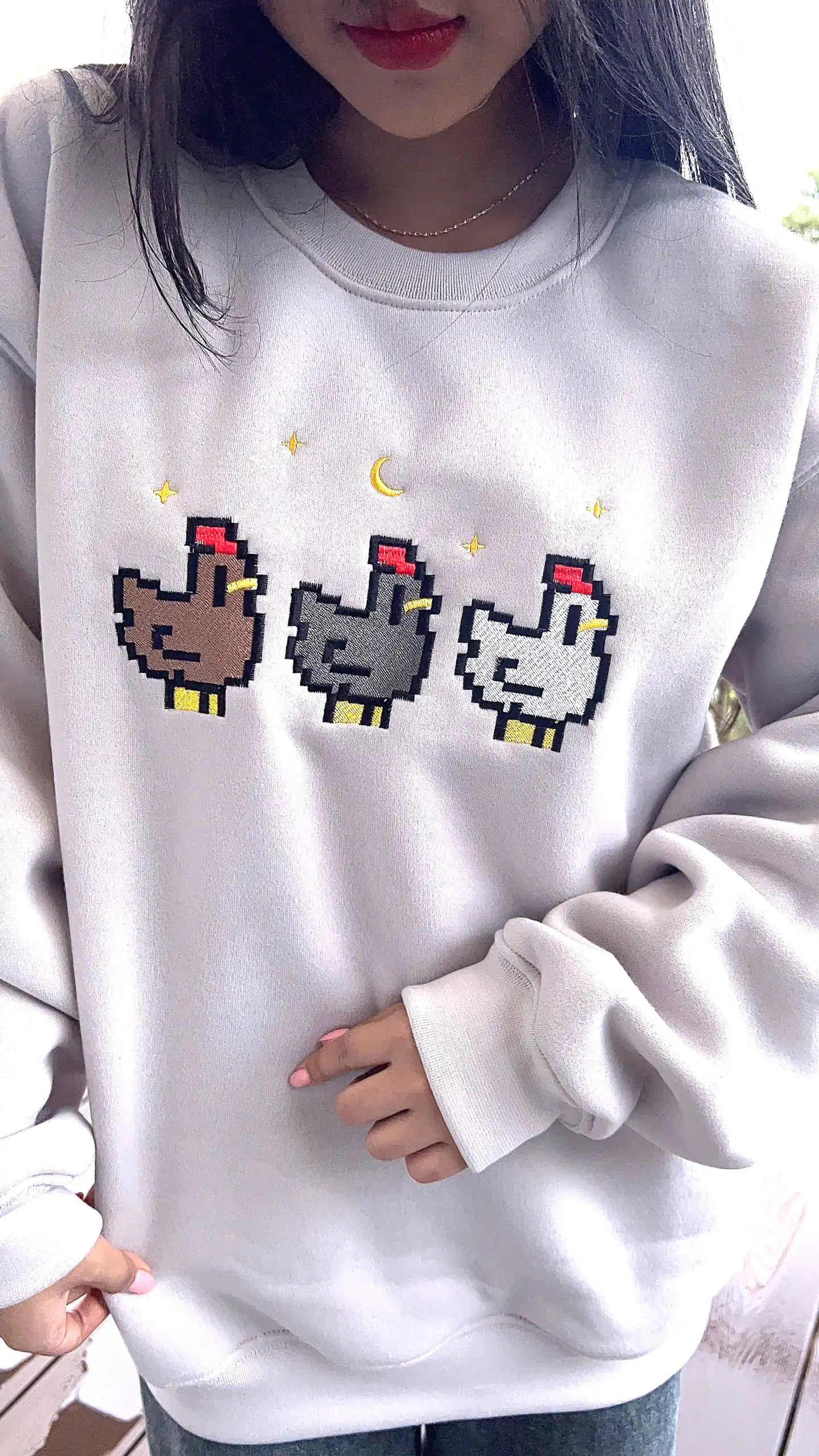 Person wearing a light gray sweatshirt with pixelated chicken designs.