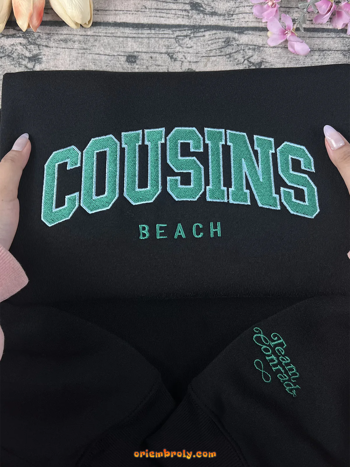 Black sweatshirt with 'COUSINS BEACH' text in green on a wooden surface.