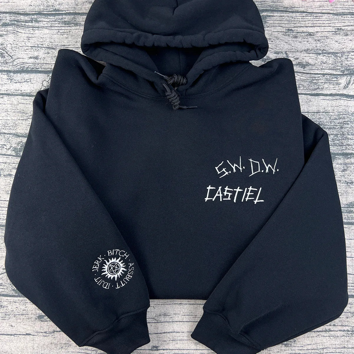 Black hoodie with white text and logo on a gray wooden surface
