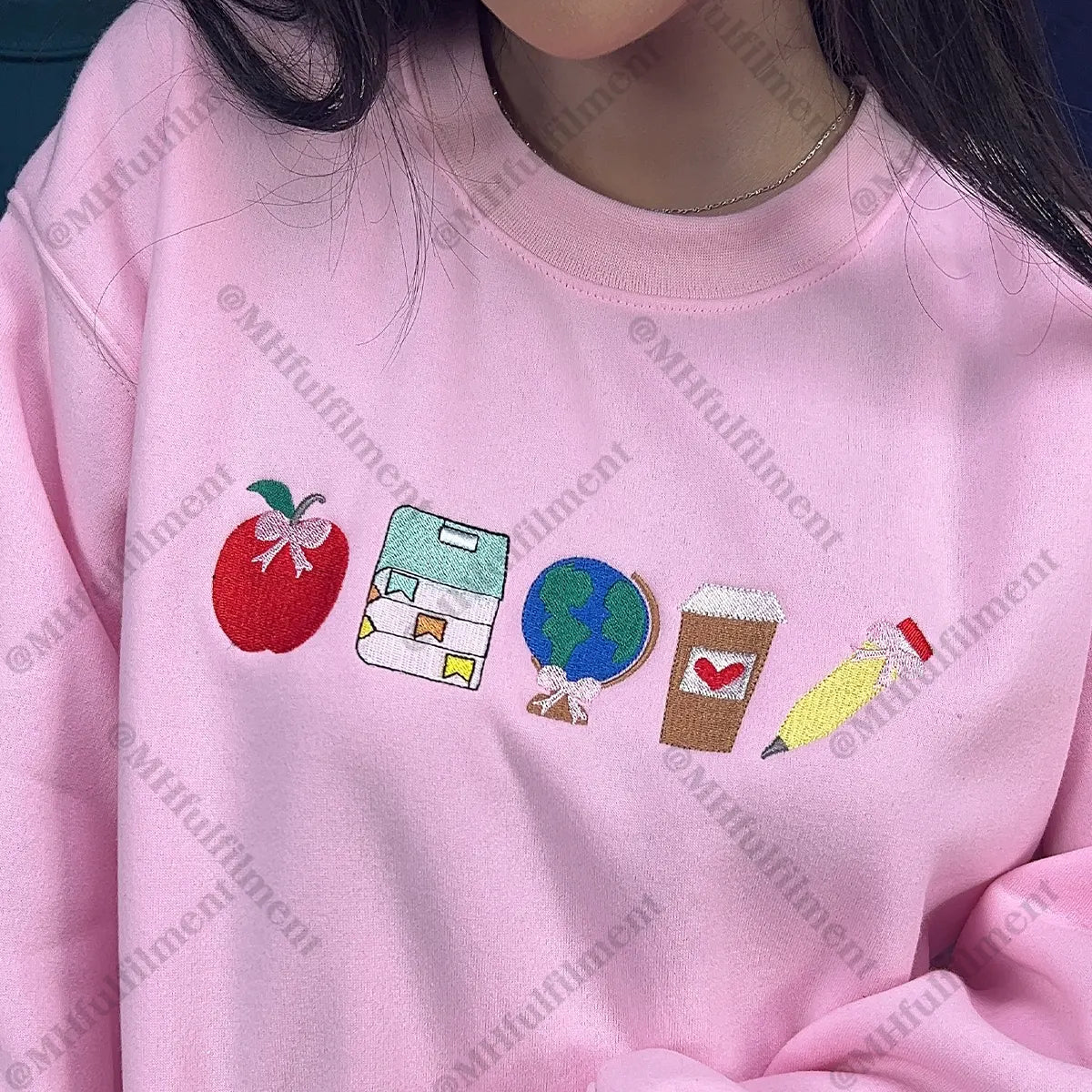 Pink sweatshirt with colorful embroidered icons on a plain background
