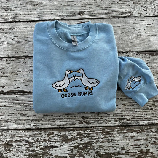 Light blue sweatshirt with goose graphic and 'Goose Bumps' text on a wooden surface