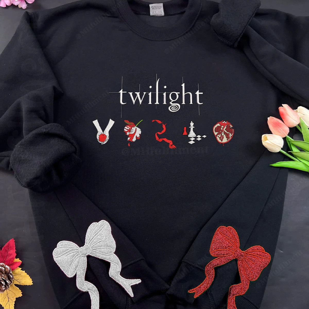Black hoodie with 'twilight' text and embroidered symbols on a dark surface with flowers.