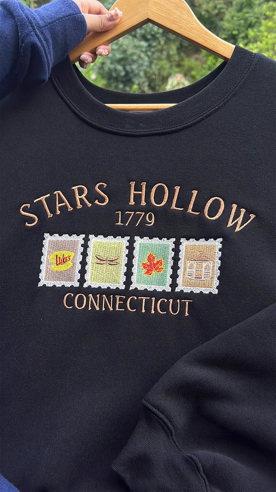 Black sweatshirt with 'Stars Hollow 1779 Connecticut' embroidery on a hanger.