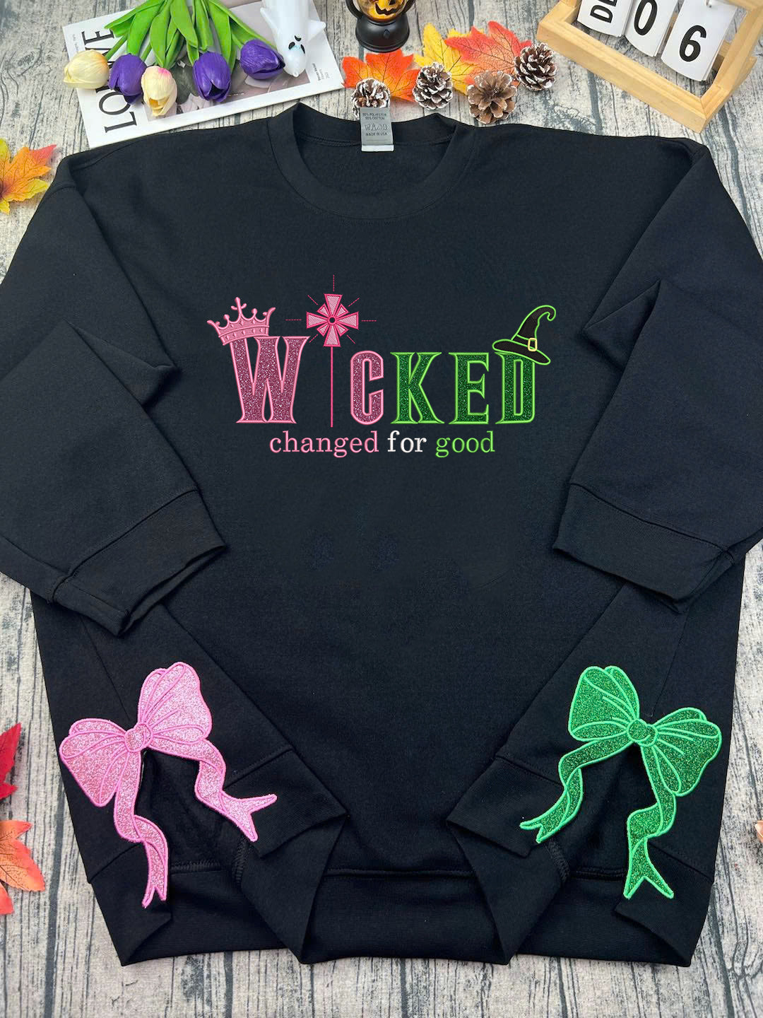 Black sweatshirt with colorful text and bows on a wooden surface