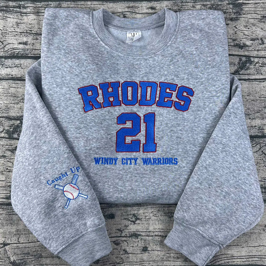 Gray sweatshirt with 'RHODES 21 Windy City Warriors' text on a wooden surface