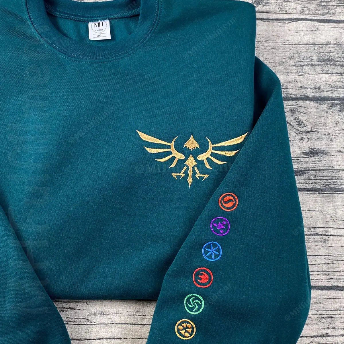 Teal hoodie with gold emblem and colorful symbols on a wooden surface