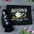 Black sweatshirt with 'Artemis II' design on a gray surface with flowers.