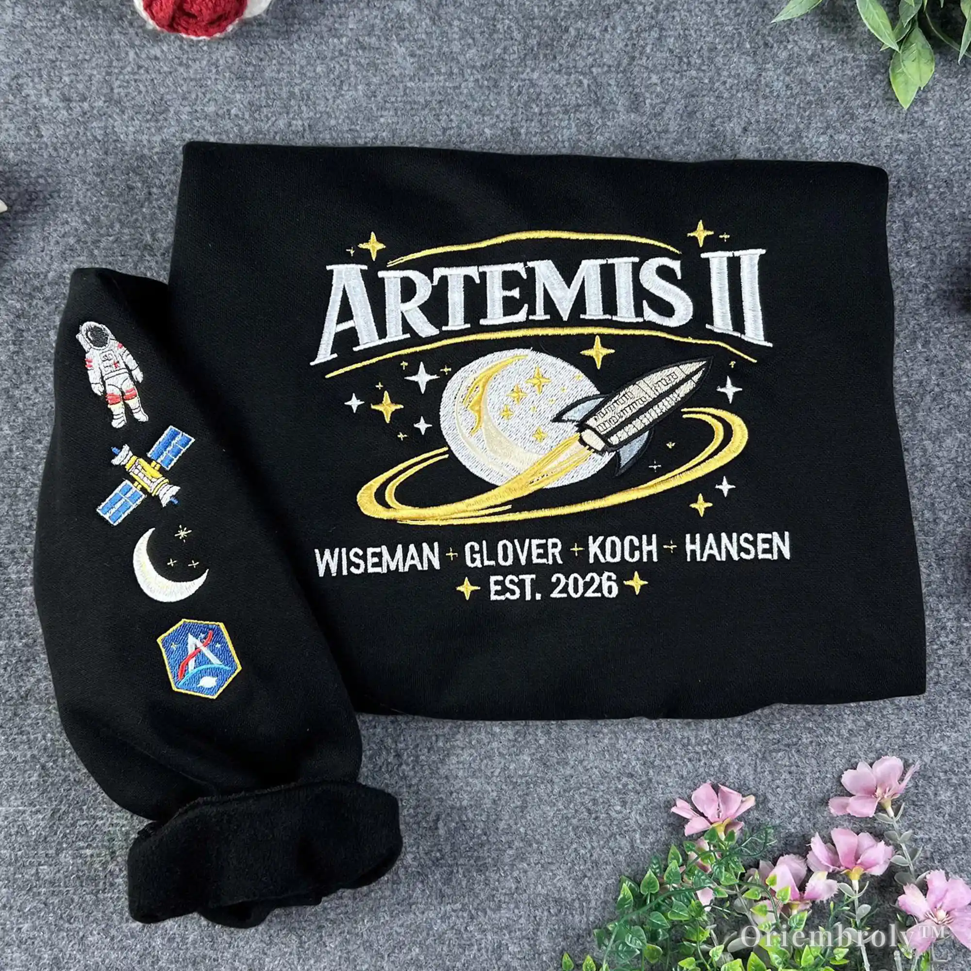 Black sweatshirt with 'Artemis II' design on a gray surface with flowers.