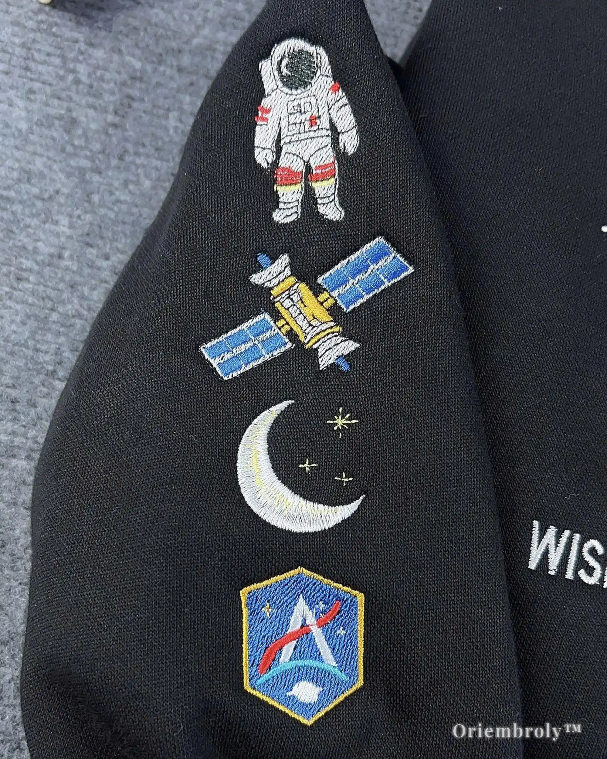 Black jacket with embroidered space-themed patches including an astronaut, satellite, moon, and shield design.