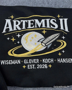 Black shirt with 'Artemis II' design featuring a rocket and stars, with names and year printed below.
