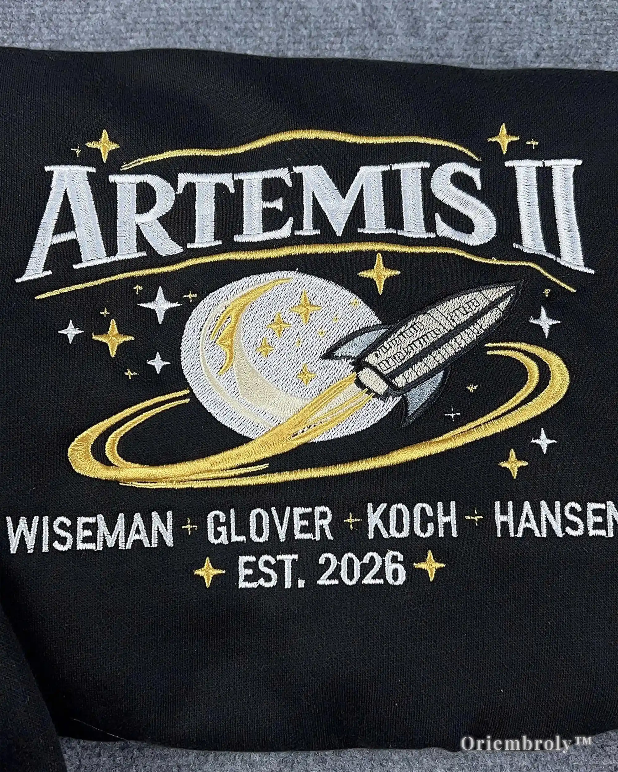 Black shirt with 'Artemis II' design featuring a rocket and stars, with names and year printed below.
