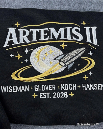 Black shirt with 'Artemis II' design featuring a rocket and stars, with names and year printed below.