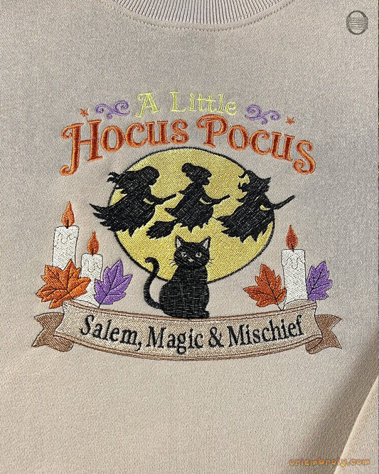 Close-up of A Little Hocus Pocus embroidery featuring a black cat, full moon, candles, and flying witches on a beige sweater
