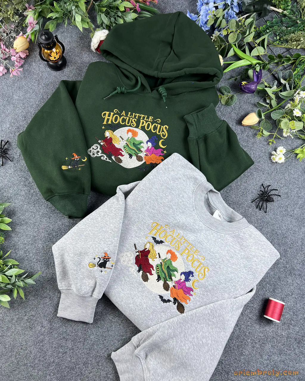 Flatlay setup of forest green hoodie and ash gray sweatshirt embroidered with A Little Hocus Pocus Sanderson sisters design and cat sleeve embroidery.