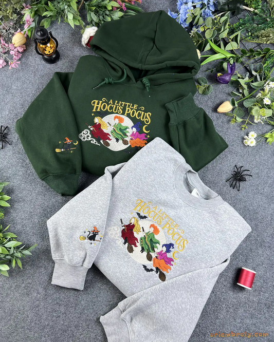 Flatlay setup of forest green hoodie and ash gray sweatshirt embroidered with A Little Hocus Pocus Sanderson sisters design and cat sleeve embroidery.