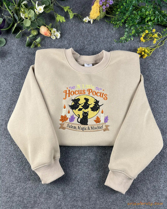 Flat lay of a sand beige Halloween crewneck sweatshirt embroidered with A Little Hocus Pocus, black cat, and flying witches