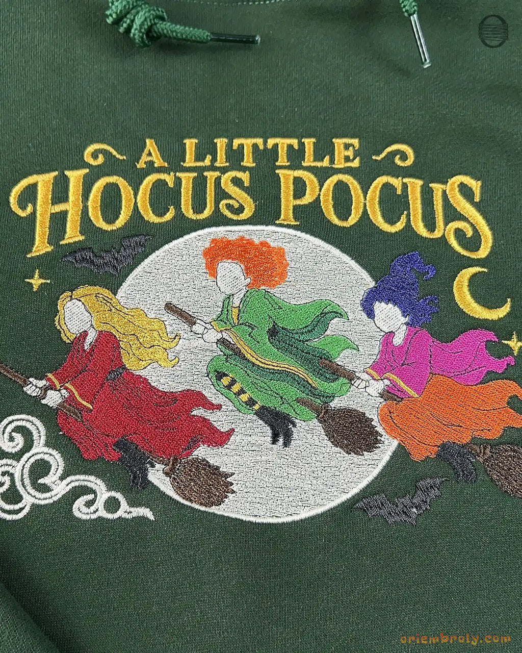 Fine embroidery detail on a forest green hoodie showing three Halloween witches flying on broomsticks under full moon.