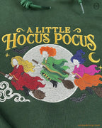 Fine embroidery detail on a forest green hoodie showing three Halloween witches flying on broomsticks under full moon.