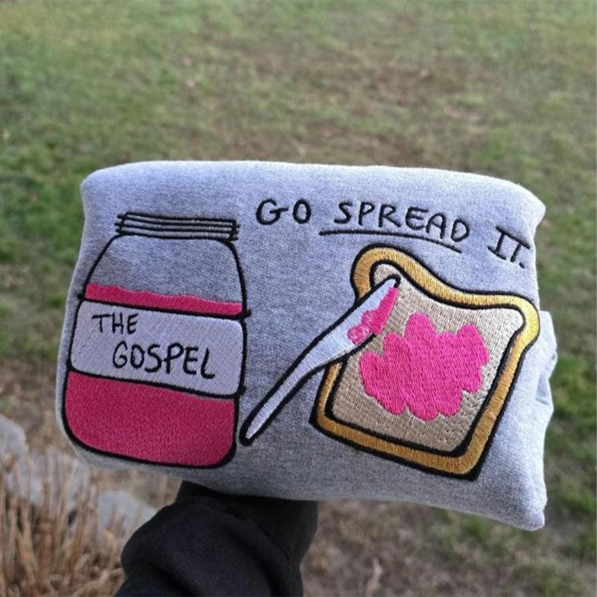 Gray pillow with illustrations of a jar labeled 'The Gospel' and a spreadable pink substance on bread, with text 'Go Spread It'.