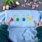 Aesthetic gamer gift idea: Light blue Stardew Valley sweater with vibrant Junimo characters.