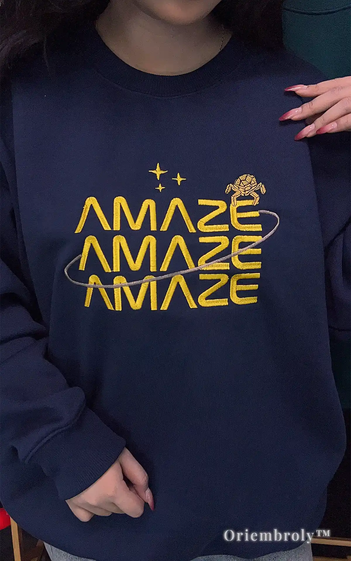 Exclusive Andy Weir book-inspired merchandise: an embroidered navy crewneck with the "Amaze Amaze Amaze" quote and orbiting stars. Perfect for sci-fi book club members and readers