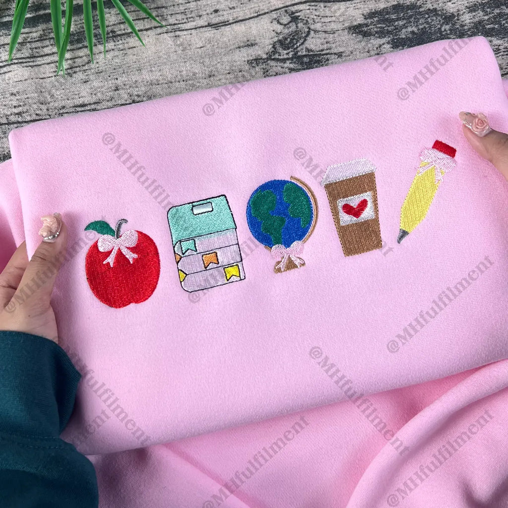 Pink fabric with embroidered icons held by a person on a wooden surface.
