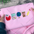Pink fabric with embroidered icons held by a person on a wooden surface.