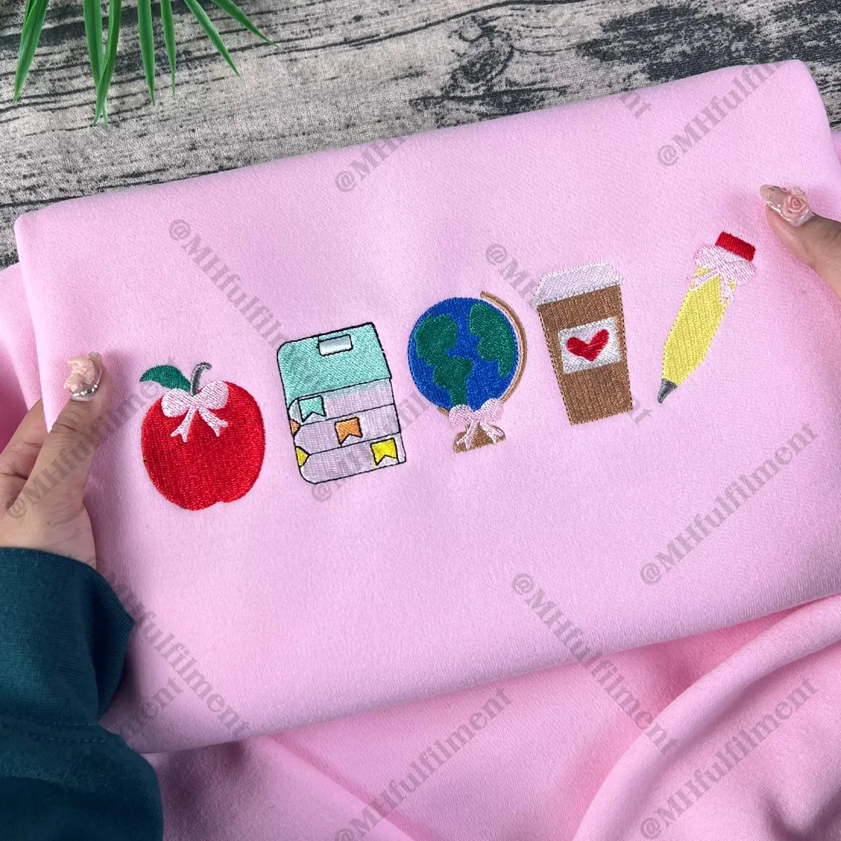 Pink fabric with embroidered icons held by a person on a wooden surface.