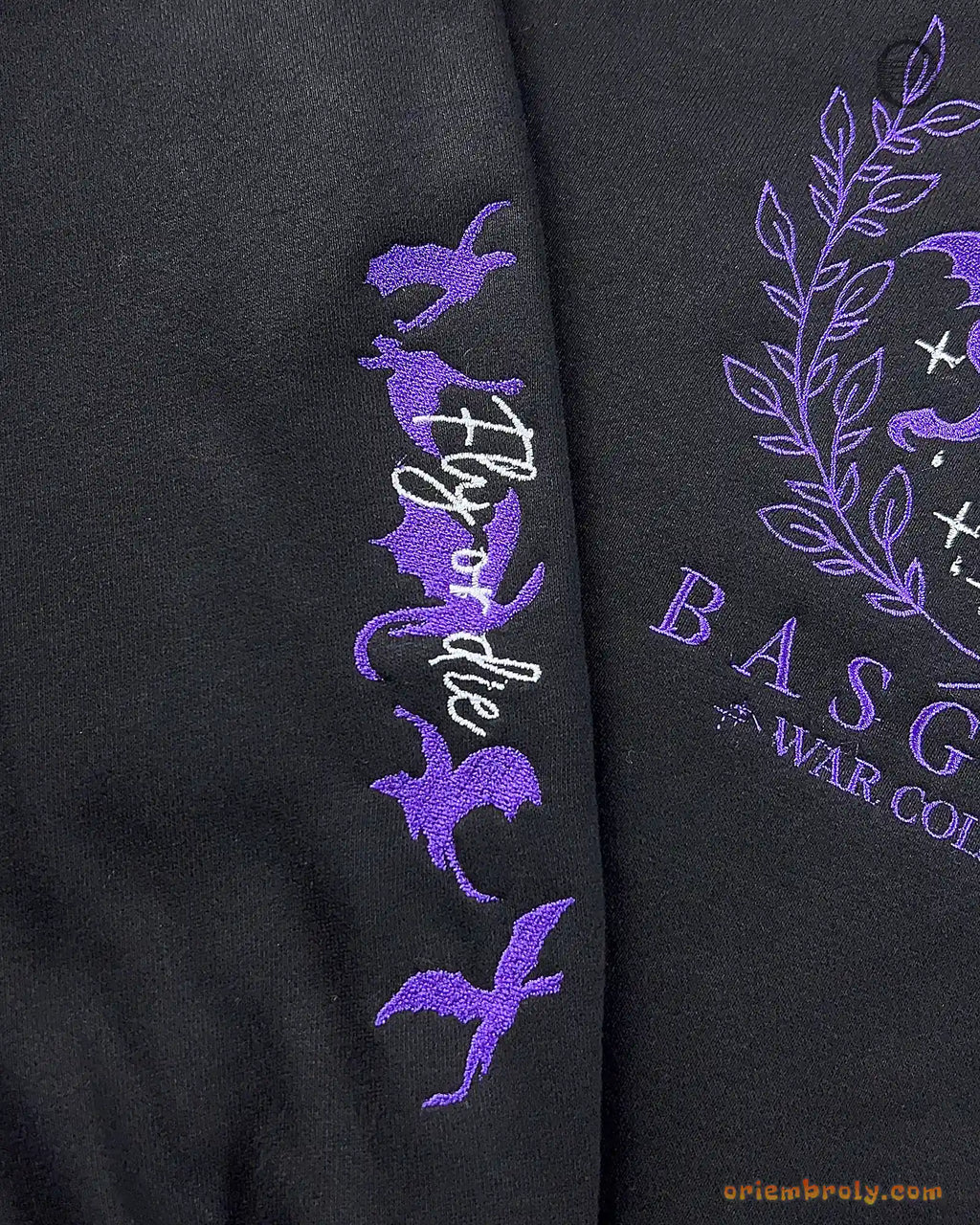 Close-up of purple flying dragons silhouette embroidered on the right sleeve of a black Fourth Wing sweatshirt