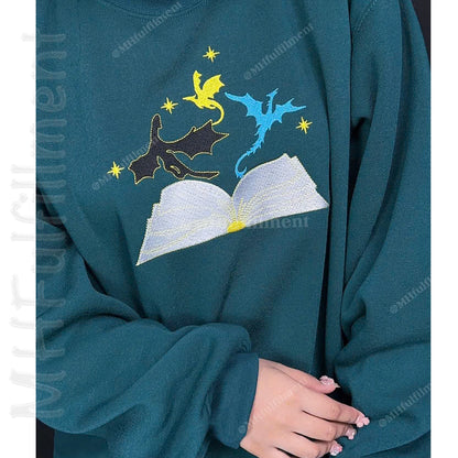 Teal sweatshirt with embroidered design of a book, dragon, and fairy on a white background.