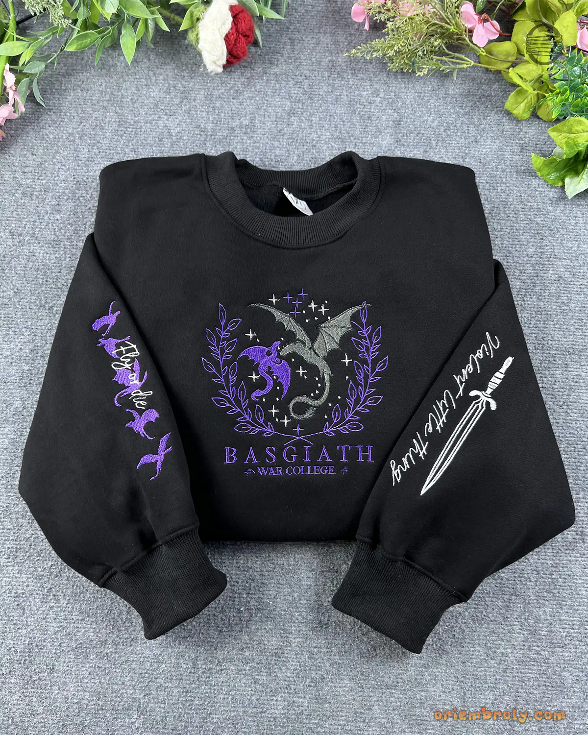 Flat lay of a black crewneck sweatshirt embroidered with Basgiath War College dragons chest emblem, dagger sleeve, and dragons sleeve