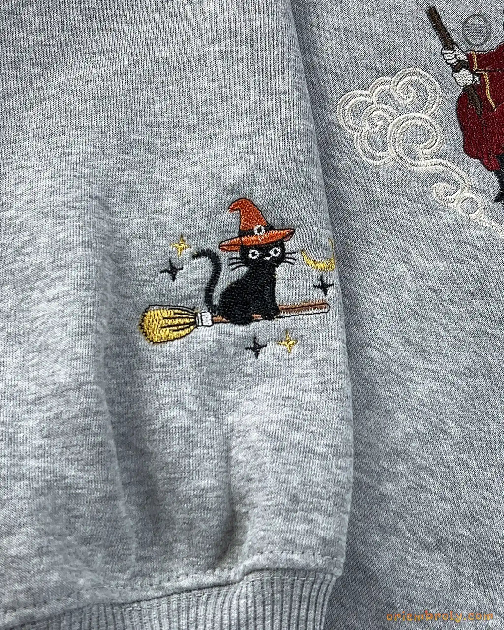 Close-up of sleeve cuff embroidery on a gray sweatshirt featuring a witch cat on a broomstick.