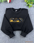 Flat lay of a black Halloween crewneck sweatshirt embroidered with cute black cats sitting in pumpkins and autumn leaves