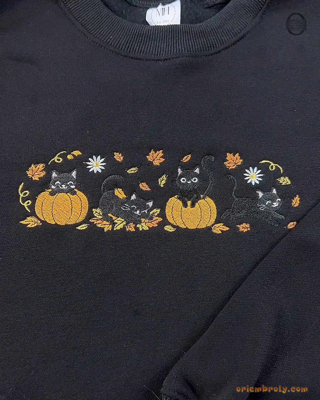 Close-up of black cats in jack-o-lantern pumpkins embroidery with fall leaves and full moon details on a black sweater