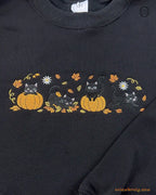 Close-up of black cats in jack-o-lantern pumpkins embroidery with fall leaves and full moon details on a black sweater