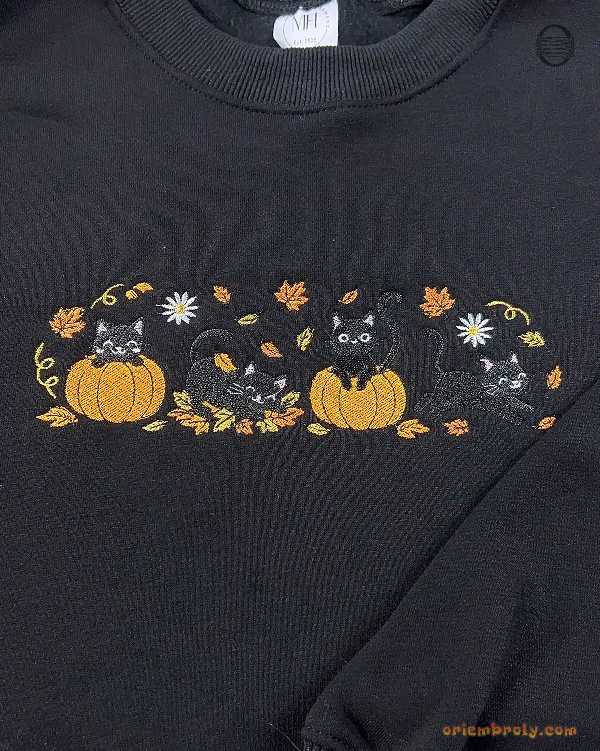 Close-up of black cats in jack-o-lantern pumpkins embroidery with fall leaves and full moon details on a black sweater