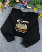 Angled flatlay view of a cozy black Harry Potter inspired Hagrid's Pumpkin Farm embroidered sweatshirt.