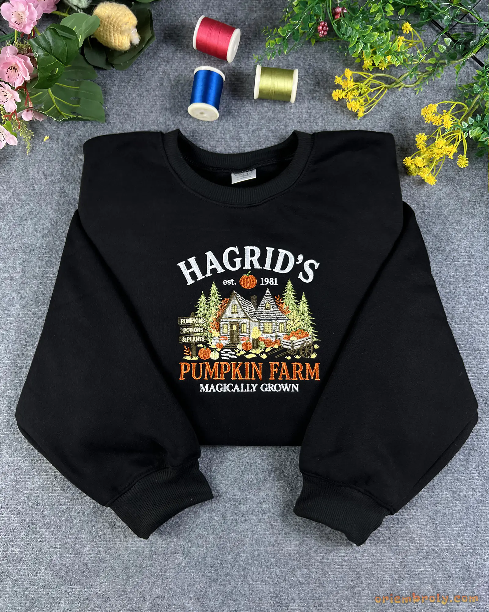 Flatlay view of a black crewneck sweatshirt embroidered with Hagrid's Pumpkin Farm Magically Grown autumn design.
