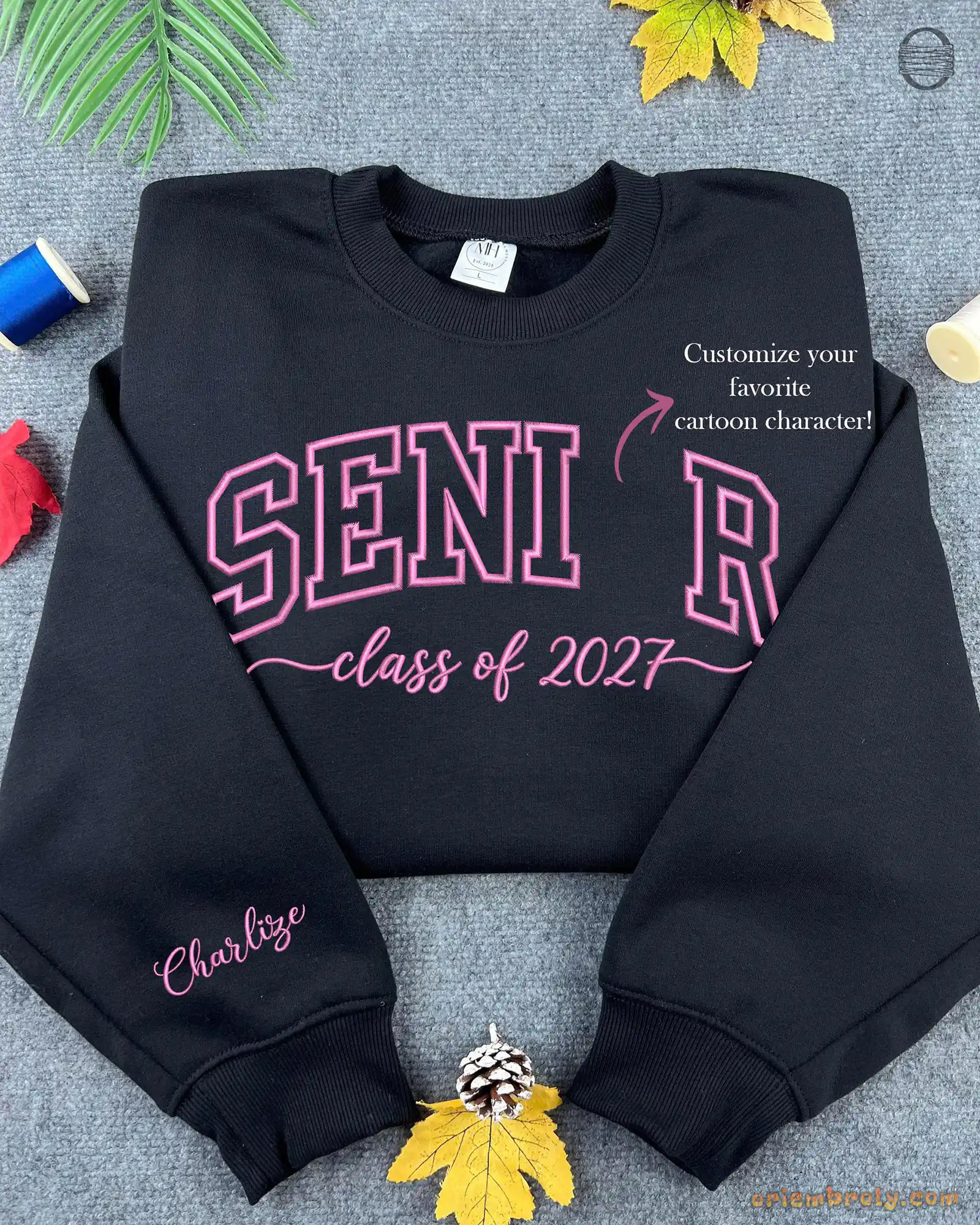 Flatlay view of a black crewneck sweatshirt embroidered with red SENIOR Class of 2027 letters and custom sleeve embroidery.
