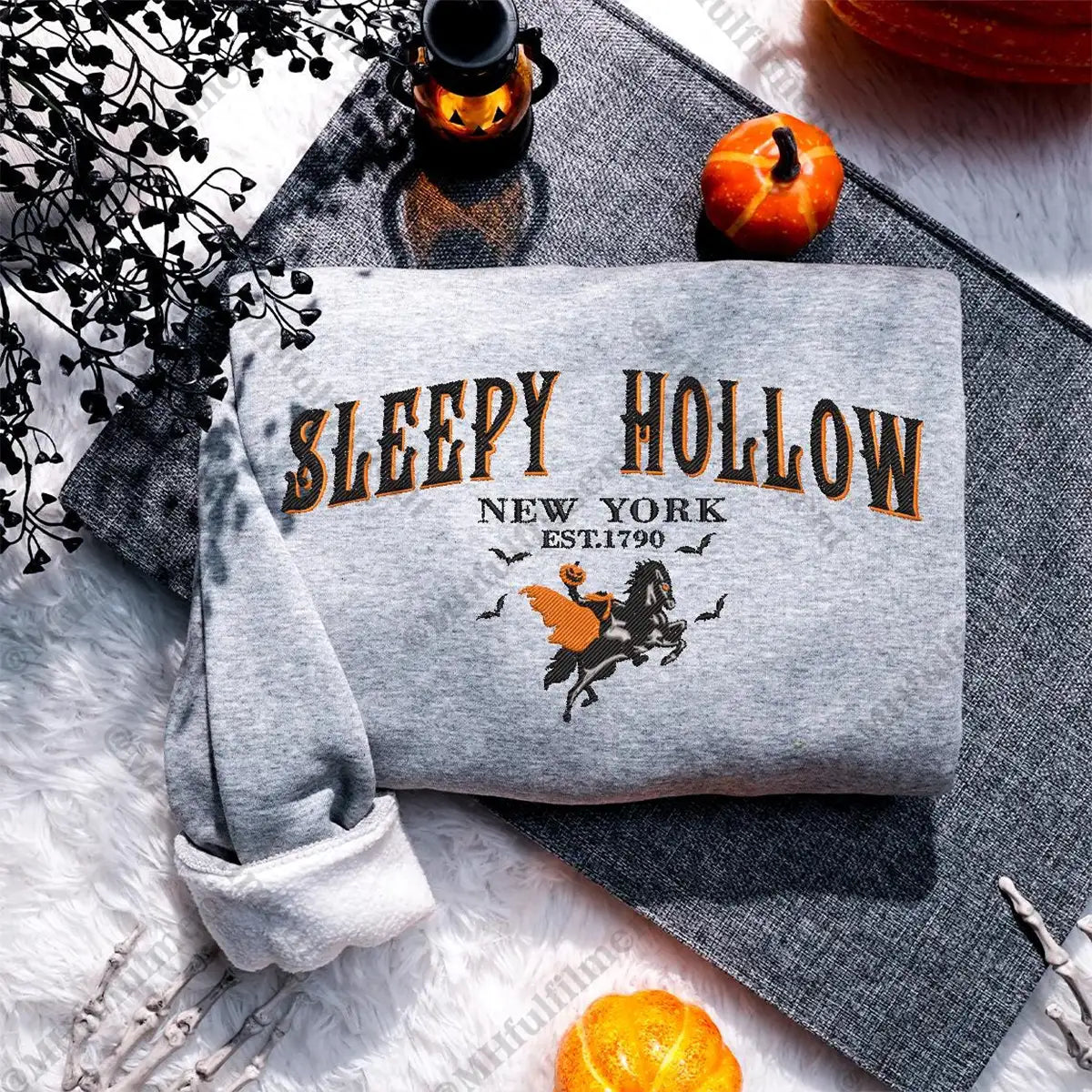 Gray sweatshirt with 'Sleepy Hollow New York' print on a textured surface with pumpkins and skeleton hands.