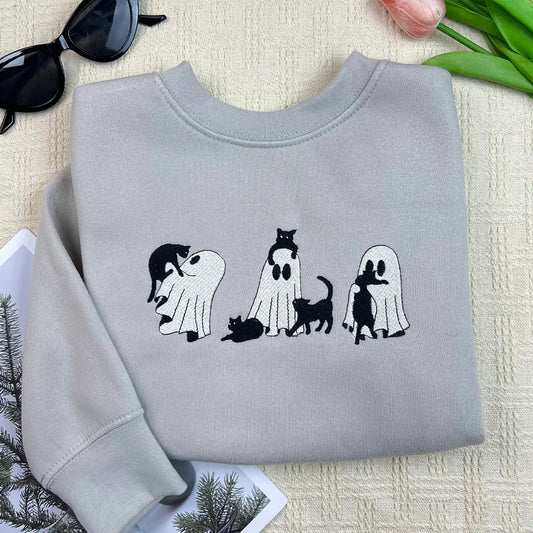 Folded gray sweatshirt with cat-themed design on a textured surface with sunglasses and flowers.