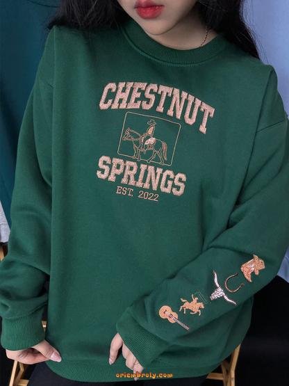 Green sweatshirt with 'Chestnut Springs' text and embroidery on a person against a blue wall.